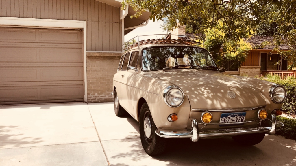 A vintage Volks-Wagon is parked in a driveway as the garage door is down